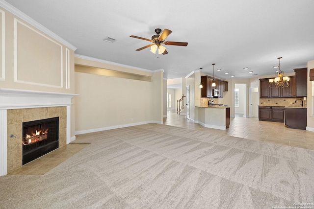 unfurnished living room with light carpet, a ceiling fan, a fireplace, a chandelier, and crown molding