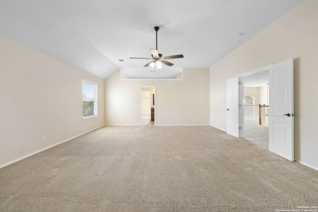 carpeted empty room featuring a ceiling fan, vaulted ceiling, and baseboards