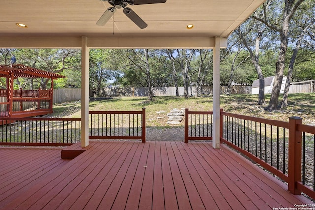 wooden terrace featuring a ceiling fan, a fenced backyard, a storage shed, and an outbuilding