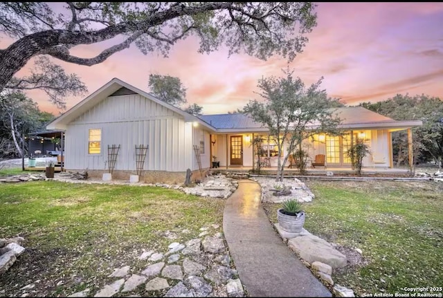 view of front of home featuring board and batten siding, a porch, a yard, and metal roof