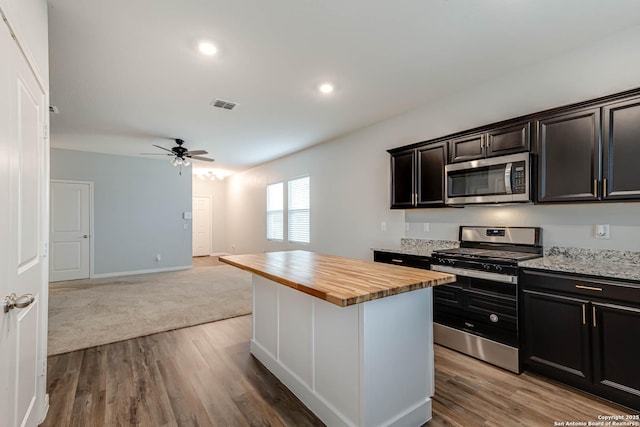 kitchen featuring appliances with stainless steel finishes, wood counters, a ceiling fan, open floor plan, and wood finished floors