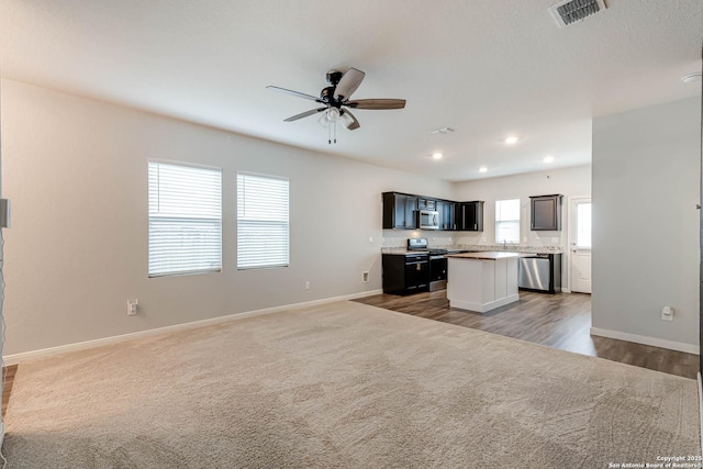 unfurnished living room featuring ceiling fan, baseboards, carpet floors, recessed lighting, and wood finished floors