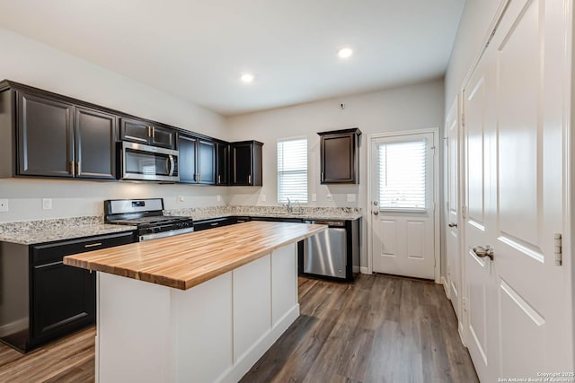 kitchen with stainless steel appliances, butcher block counters, dark wood finished floors, recessed lighting, and a kitchen island