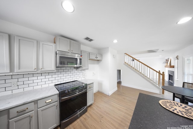 8201 Bluff Bnd, San Antonio, TX 78250 - kitchen with stainless steel microwave, range with electric stovetop, gray cabinets, tasteful backsplash, and a fireplace
