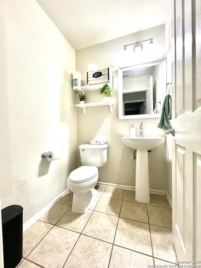 half bathroom featuring toilet, a textured ceiling, tile patterned floors, baseboards, and a textured wall