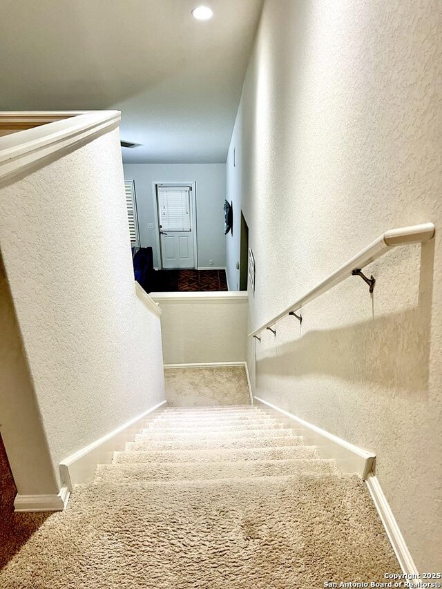 stairs featuring a textured wall, baseboards, and carpet floors
