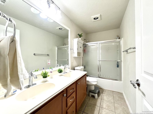 bathroom featuring toilet, double vanity, tile patterned floors, bath / shower combo with glass door, and baseboards