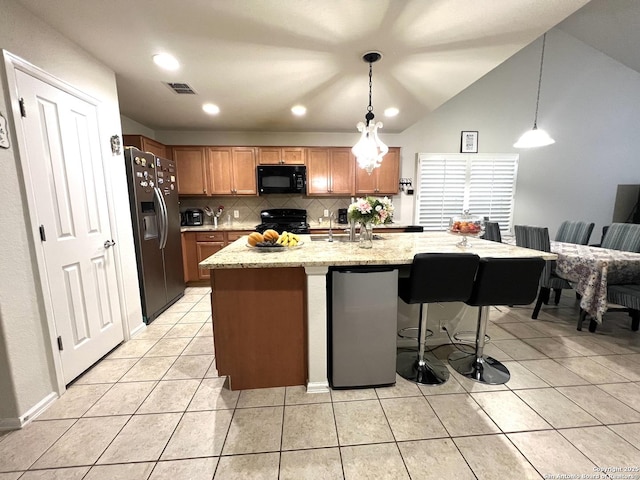 kitchen featuring black appliances, tasteful backsplash, light tile patterned flooring, light stone counters, and a kitchen breakfast bar