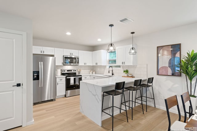 1108 S Gevers St, San Antonio, TX 78203 - kitchen featuring appliances with stainless steel finishes, a peninsula, a sink, light wood-style floors, and a kitchen breakfast bar