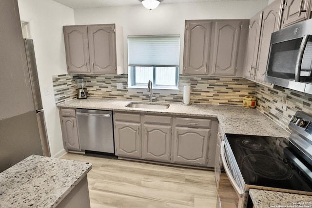 kitchen with appliances with stainless steel finishes, a sink, gray cabinetry, and backsplash