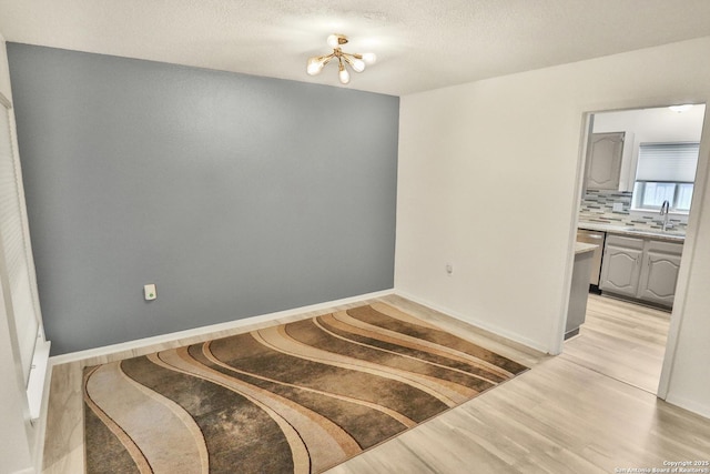 unfurnished dining area with a sink, a chandelier, light wood finished floors, baseboards, and a textured ceiling
