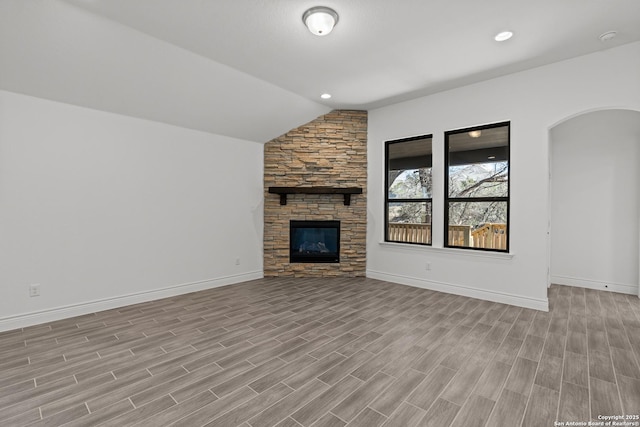 2171 Oak Run Pkwy, New Braunfels, TX 78132 - unfurnished living room featuring vaulted ceiling, baseboards, light wood-style floors, a stone fireplace, and arched walkways