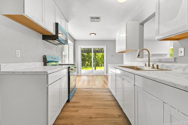 kitchen with stainless steel electric range oven, a sink, white cabinets, light wood-style floors, and light stone counters