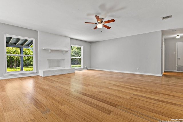 unfurnished living room featuring a ceiling fan, light wood-type flooring, baseboards, and a brick fireplace