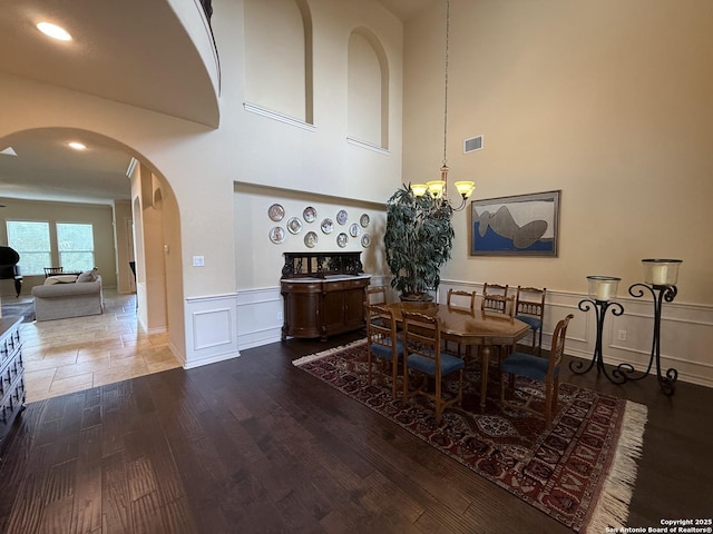 25215 Estancia, San Antonio, TX 78260 - dining room with arched walkways, a decorative wall, a chandelier, wood finished floors, and wainscoting