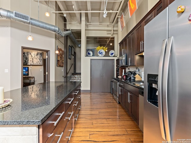 1339 S Flores St Unit 103, San Antonio, TX 78204 - kitchen with stainless steel appliances, a towering ceiling, light wood finished floors, dark brown cabinetry, and pendant lighting