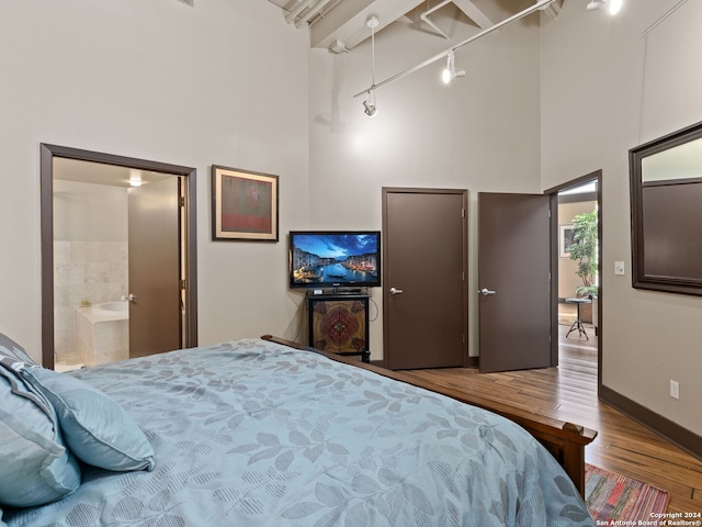 1339 S Flores St Unit 103, San Antonio, TX 78204 - bedroom featuring a high ceiling, wood finished floors, baseboards, rail lighting, and ensuite bath