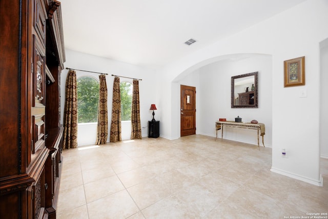 unfurnished room with arched walkways, light tile patterned flooring, and baseboards