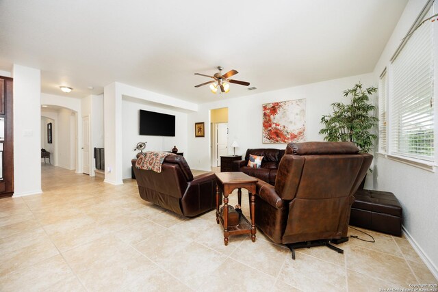 living room with arched walkways, a ceiling fan, baseboards, and light tile patterned floors