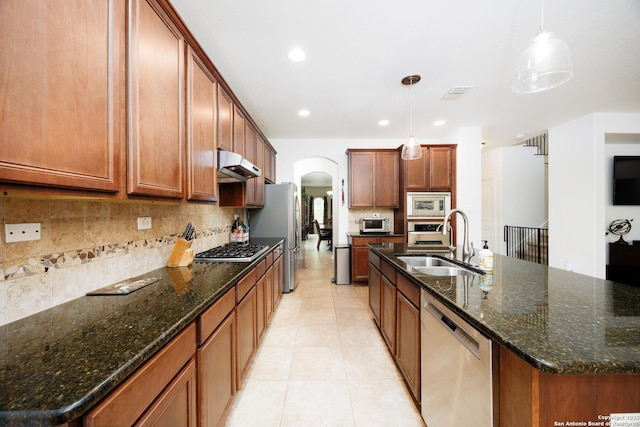 kitchen featuring appliances with stainless steel finishes, a sink, under cabinet range hood, arched walkways, and decorative backsplash