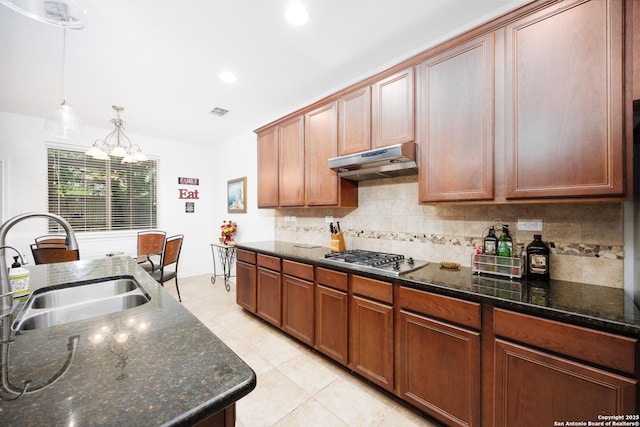 kitchen featuring under cabinet range hood, stainless steel gas cooktop, a sink, a chandelier, and decorative backsplash