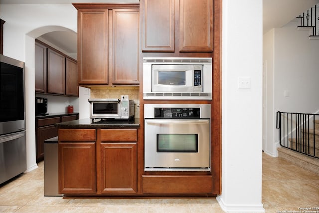 kitchen with appliances with stainless steel finishes, tasteful backsplash, baseboards, light tile patterned floors, and arched walkways