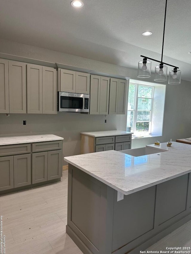 109 Sutton Pl, Uvalde, TX 78801 - kitchen featuring stainless steel microwave, gray cabinets, decorative light fixtures, light stone counters, and recessed lighting
