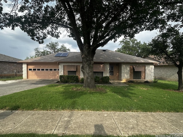 view of front of house featuring driveway, a garage, a front lawn, roof mounted solar panels, and brick siding