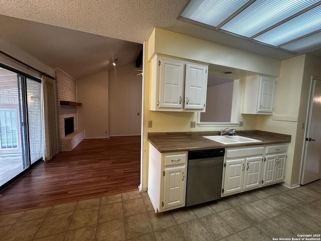 kitchen with stainless steel dishwasher, a sink, dark countertops, white cabinetry, and a fireplace