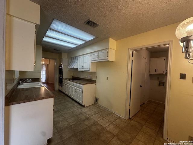 kitchen with premium range hood, dark countertops, a sink, white cabinets, and double oven