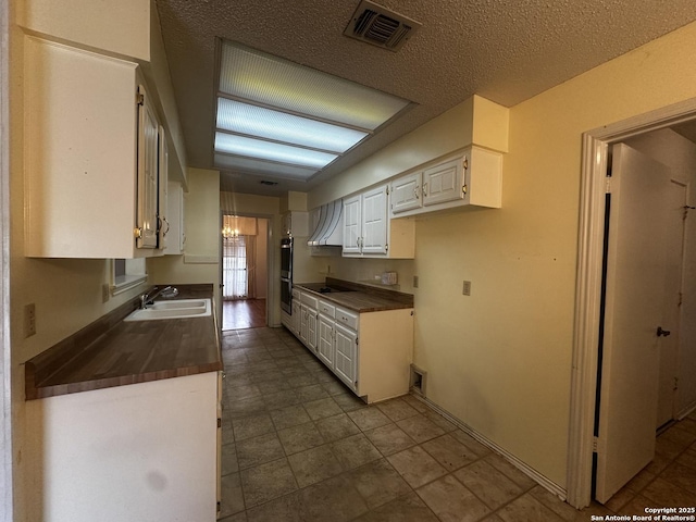 kitchen featuring dark countertops, white cabinets, a sink, wall chimney exhaust hood, and a textured ceiling