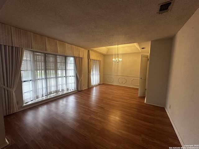 spare room featuring a chandelier, a textured ceiling, wood finished floors, and baseboards