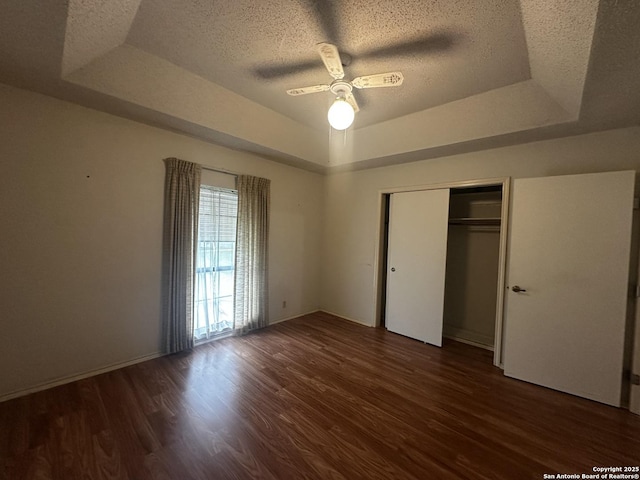 unfurnished bedroom featuring a tray ceiling, a textured ceiling, wood finished floors, a closet, and a ceiling fan