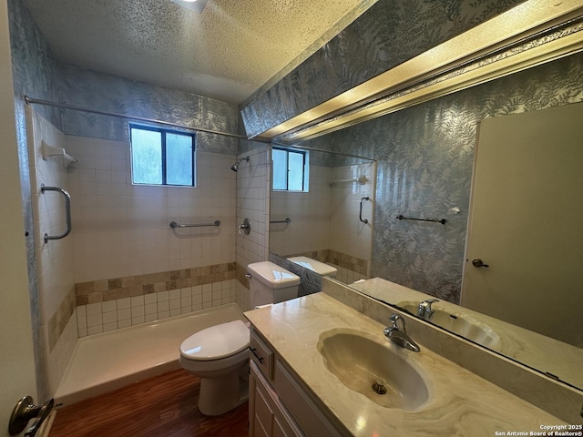 bathroom with wood finished floors, toilet, tiled shower, vanity, and a textured ceiling