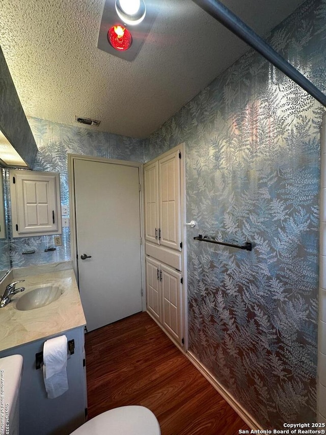 bathroom featuring wallpapered walls, wood finished floors, vanity, a textured ceiling, and toilet
