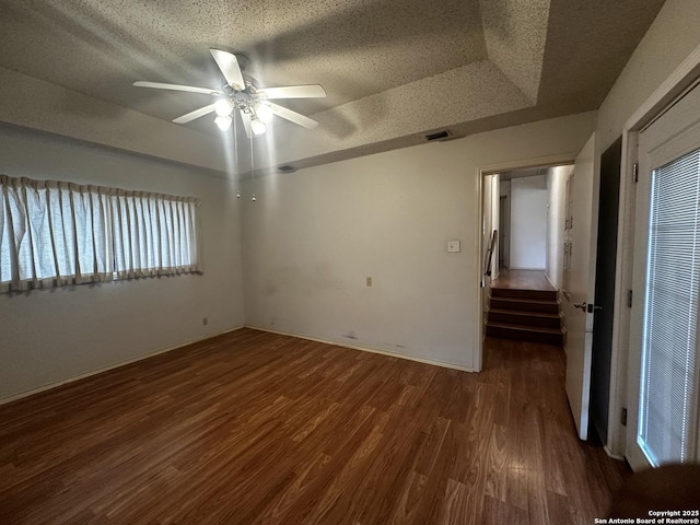 empty room featuring wood finished floors, a textured ceiling, a ceiling fan, stairway, and a raised ceiling
