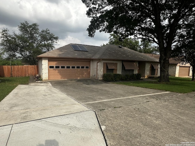 ranch-style home with roof mounted solar panels, driveway, an attached garage, and brick siding