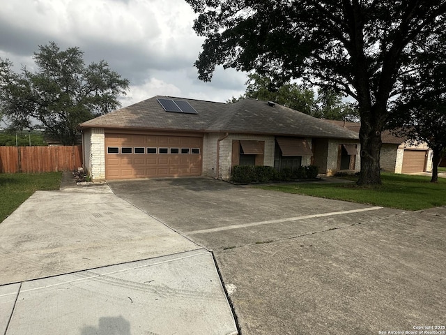 ranch-style home with roof mounted solar panels, a garage, concrete driveway, brick siding, and roof with shingles