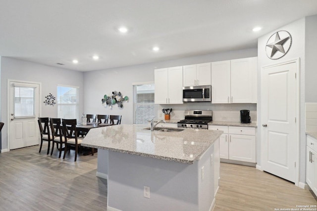 8911 Rancher Pl, Seguin, TX 78155 - kitchen with stainless steel appliances, a sink, light wood-style flooring, white cabinetry, and backsplash