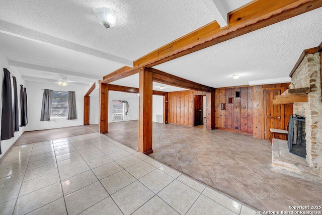 235 Altgelt, San Antonio, TX 78201 - unfurnished living room with a textured ceiling, a stone fireplace, wood walls, ceiling fan, and beamed ceiling