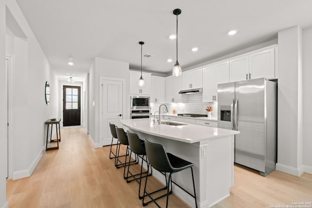 kitchen featuring stainless steel appliances, a sink, under cabinet range hood, light wood-style flooring, and baseboards
