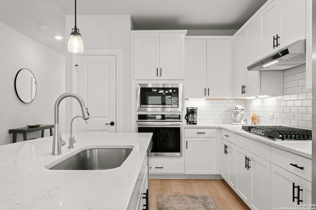 kitchen featuring stainless steel appliances, under cabinet range hood, a sink, light wood finished floors, and white cabinetry