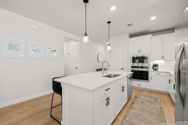 kitchen with appliances with stainless steel finishes, a sink, light wood finished floors, backsplash, and recessed lighting