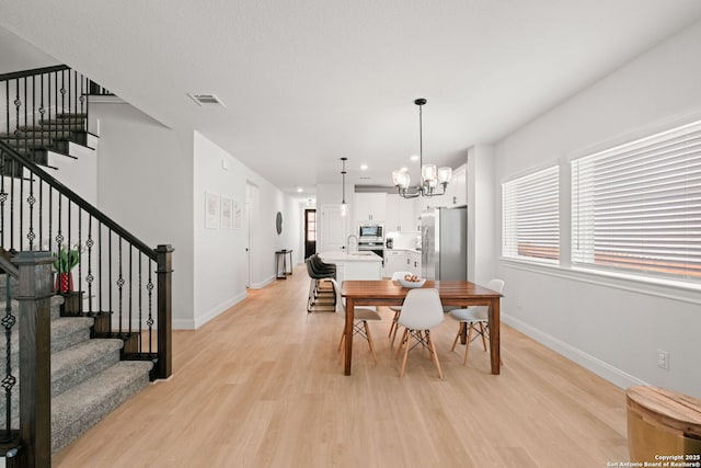 dining room with light wood-style floors, stairway, a chandelier, and baseboards