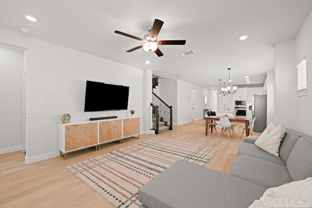 living room featuring stairs, light wood finished floors, a ceiling fan, a chandelier, and recessed lighting