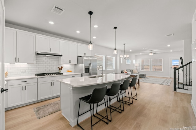 kitchen featuring stainless steel fridge, a sink, gas stovetop, under cabinet range hood, and white cabinetry