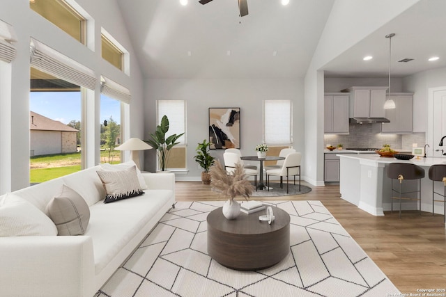 living room featuring high vaulted ceiling, light wood-type flooring, recessed lighting, a ceiling fan, and baseboards