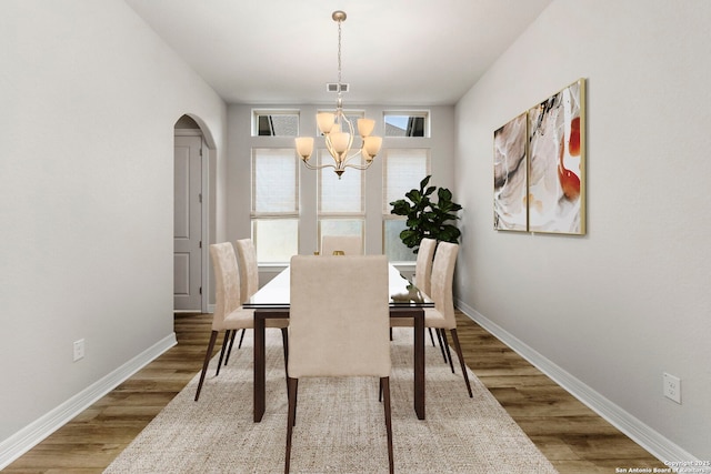 dining room with a chandelier, arched walkways, wood finished floors, and baseboards