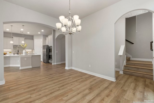 unfurnished living room with arched walkways, recessed lighting, light wood-style flooring, baseboards, and a chandelier