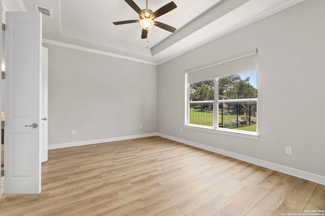 empty room with ceiling fan, a tray ceiling, light wood-type flooring, baseboards, and ornamental molding